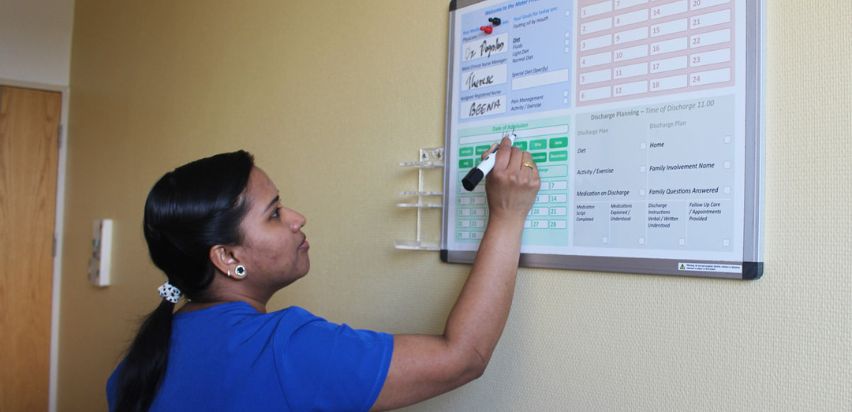 Beena Sasi is using a black marker to write patient information onto a white board inside a patient room.