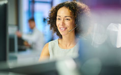 billing-and-insurance A woman is sitting at a desk and is looking at a computer while speaking through a headset.