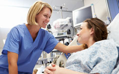 FAQs A female nurse is leaning toward and touching the head of a female patient who is lying in a hospital bed.