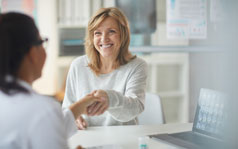 your-appointment A woman is smiling and shaking the hand of a female doctor sitting across from her.