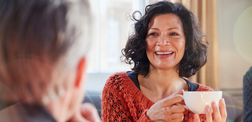 A woman smiling, looking at a man, holding a cup