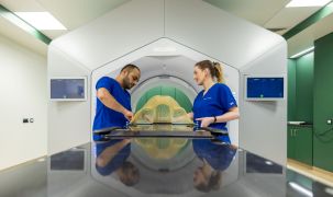 Two medical professionals are standing on either side of the bed and are working with the Varian Halcyon™ Radiotherapy machine.
